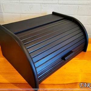 May include: Black wooden bread box with a roll-top lid. The lid has a slatted design and a small handle.