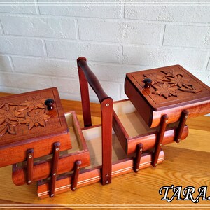 May include: A wooden sewing box with three compartments and a handle. The box features a carved floral design on the lids and is made from rich brown wood.