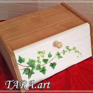 Op de afbeelding: Een houten broodtrommel met een wit deksel met een groen klimoprankontwerp. Het deksel heeft een kleine houten knop. De tekst "TARA.art" is zichtbaar onderaan de afbeelding.