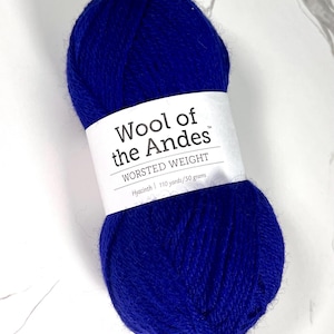 Può includere: Un gomitolo di filato blu giacinto della collezione Wool of the Andes, peso worsted. L'etichetta bianca indica 100.58 metri per 50 grammi. Il filato è di un colore vivace e uniforme, ideale per progetti di maglia e uncinetto.