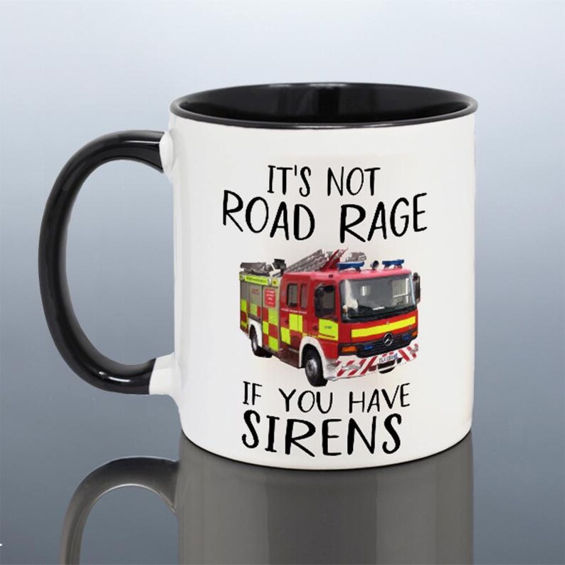 May include: White ceramic mug with a black handle and interior. The mug features a red and yellow fire truck graphic and the text "It's Not Road Rage If You Have Sirens" in black.