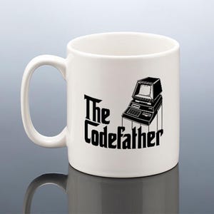 May include: White ceramic mug featuring a black and white image of a vintage computer and the text "The Codefather".