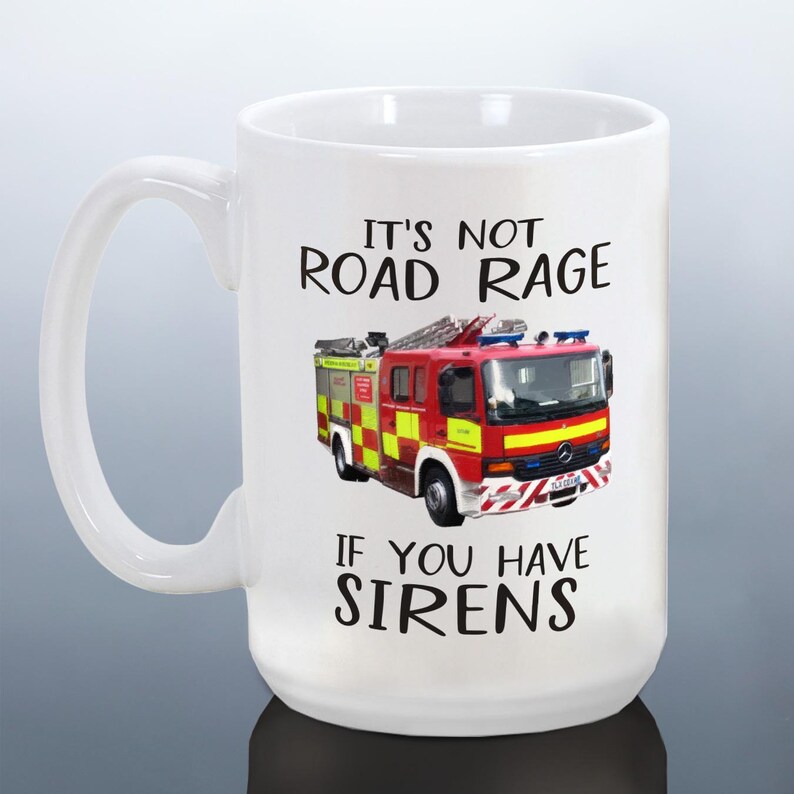 May include: White ceramic mug featuring a red and yellow fire truck graphic. The mug has the text "IT'S NOT ROAD RAGE IF YOU HAVE SIRENS" in black. The mug has a large handle.