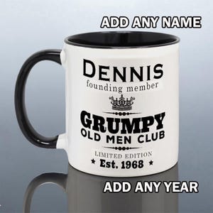May include: A white ceramic mug with a black handle and interior. The front features black text reading "DENNIS founding member," a crown icon, "GRUMPY OLD MEN CLUB," and "LIMITED EDITION Est. 1968." The text "ADD ANY NAME" and "ADD ANY YEAR" is visible.