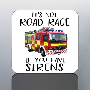 May include: A square coaster with rounded corners featuring a red and yellow fire truck illustration. The text reads "IT'S NOT ROAD RAGE IF YOU HAVE SIRENS" in black font. The coaster has a glossy finish.