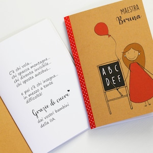 May include: A brown notebook with a red polka dot border and the text "MAESTRA Bruna" on the cover. The notebook has a drawing of a stick figure teacher holding a chalkboard with the letters "ABC DEF" written on it. The teacher is wearing a red dress and has a red balloon tied to her hand.