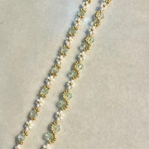May include: A delicate necklace with alternating white and light green beads. The beads are strung on a gold chain.