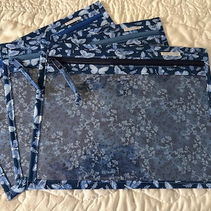 May include: Three rectangular zip pouches featuring a clear vinyl front panel and a dark blue fabric border patterned with white butterflies and floral motifs. Each pouch includes a dark blue zip closure and a small fabric brand label.