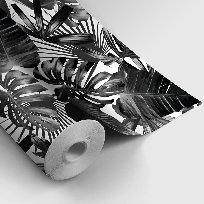May include: A roll of wallpaper featuring a black and white tropical leaf pattern. The design includes large monstera leaves, palm fronds, and other foliage against a white background. The wallpaper is partially unrolled, revealing the paper's core.