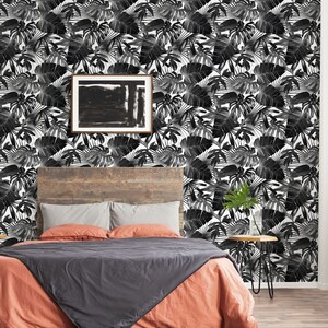May include: A bedroom with a tropical theme. The focal point is a bed with an orange comforter and a gray blanket. The headboard is made of wood. The wall is covered in black and white tropical leaf wallpaper. A framed abstract painting hangs on the wall.