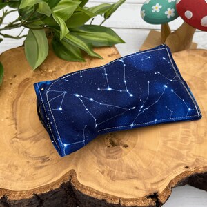 Puede incluir: Una bolsa de tela azul con un patr&oacute;n de constelaci&oacute;n blanca. La bolsa est&aacute; doblada y sentada sobre una superficie de madera.