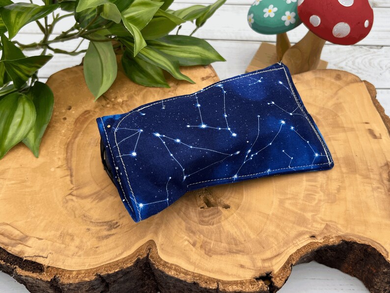 Puede incluir: Una bolsa de tela azul con un patr&oacute;n de constelaci&oacute;n blanca. La bolsa est&aacute; doblada y sentada sobre una superficie de madera.
