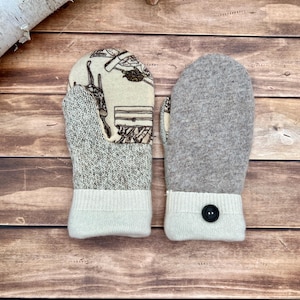 May include: A pair of mittens featuring a cream-colored fabric with a brown line-art pattern on one side and solid heathered gray wool on the other. The cuffs are made of ribbed cream knit fabric, with a single black button on one cuff.