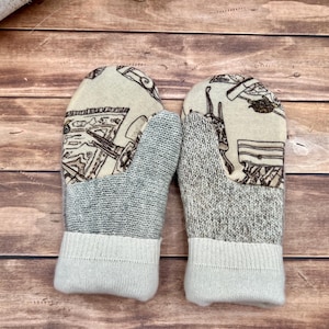 May include: A pair of mittens featuring a cream-colored fabric upper with a brown line-art pattern of various objects. The lower section is made of a textured gray knit fabric, finished with a solid cream-colored ribbed knit cuff.