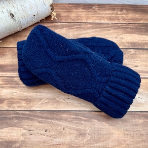 May include: A pair of dark navy blue knit mittens featuring a textured cable knit pattern on the back of the hand and a ribbed cuff at the wrist. The mittens are constructed from a solid-colored yarn and have a consistent deep blue tone.