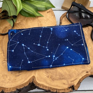 Puede incluir: Un estuche para gafas de tela azul con un patr&oacute;n de constelaci&oacute;n blanca. El estuche tiene un borde blanco cosido.
