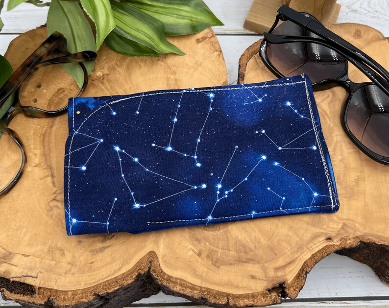 Puede incluir: Un estuche para gafas de tela azul con un patr&oacute;n de constelaci&oacute;n blanca. El estuche tiene un borde blanco cosido.