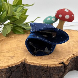 Puede incluir: Un estuche para gafas de tela azul y dorada con un patr&oacute;n estrellado, doblado y colocado sobre una superficie de madera.