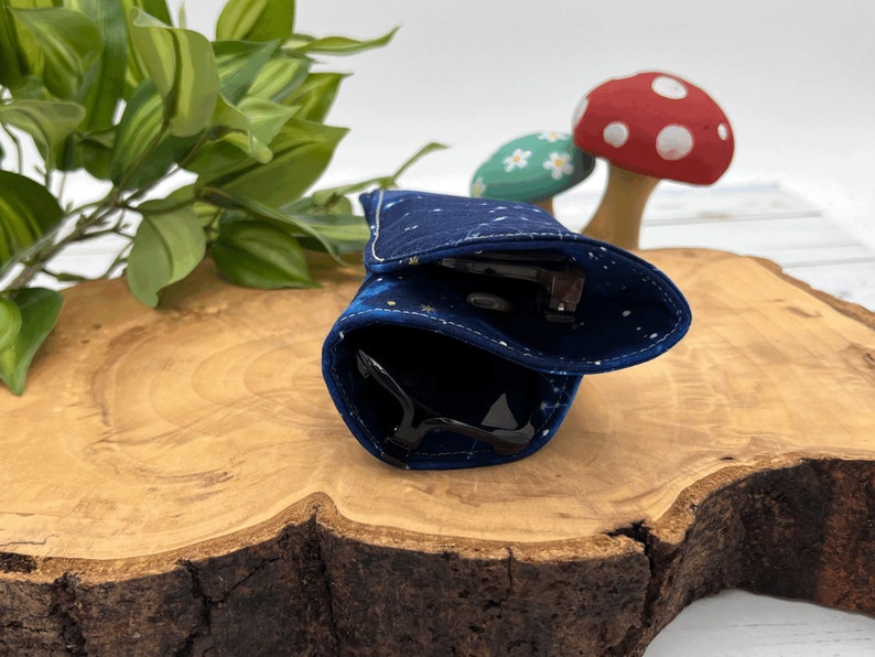 Puede incluir: Un estuche para gafas de tela azul y dorada con un patr&oacute;n estrellado, doblado y colocado sobre una superficie de madera.