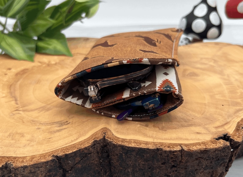 Op de afbeelding: Een bruine brillenkoker met een vogelpatroon en een voering met een patroon in zuidwestelijke stijl. De koker is open en onthult een bril en een set sleutels. De koker is gemaakt van een zacht, getextureerd materiaal.