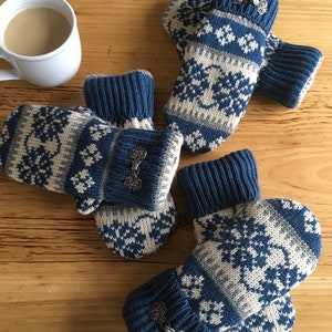 May include: A pair of blue and white knitted mittens with a snowflake pattern and silver metal accents. The mittens are on a wooden surface.