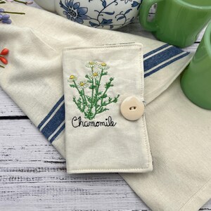 This tea wallet has a beautiful machine embroidery chamomile plant with green leaves and white flowers with a yellow middle and the word chamomile handwritten underneath the plant