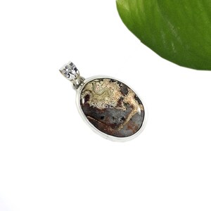 Puede incluir: Un colgante de plata con una piedra de &aacute;gata marr&oacute;n, blanca y beige con un patr&oacute;n de remolino. La piedra es de forma ovalada y est&aacute; engastada en un bisel de plata.