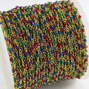 May include: A gold chain with red, green, and blue faceted beads. The chain is wound around a spool.