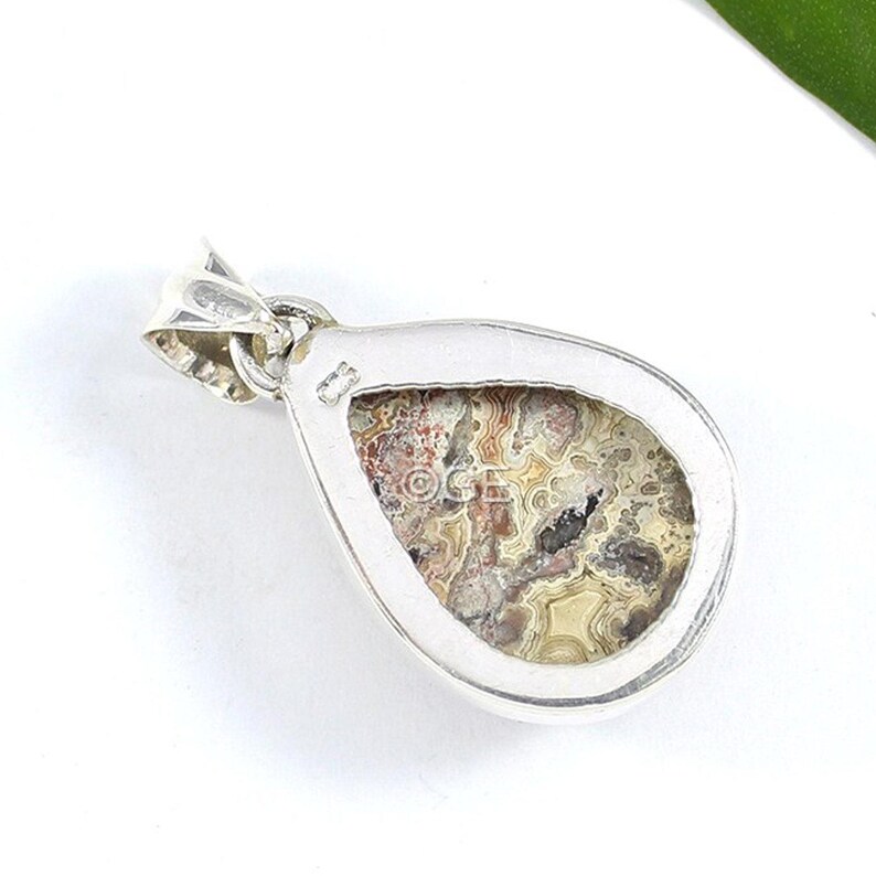 Puede incluir: Un colgante de plata con una piedra en forma de l&aacute;grima que presenta un patr&oacute;n de &aacute;gata colorido. La piedra est&aacute; engastada en un bisel de plata y tiene un aro de suspensi&oacute;n de plata.