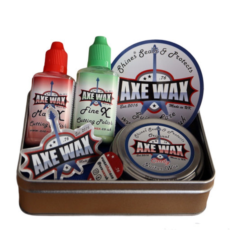 May include: A set of guitar care products in a silver tin. The set includes a bottle of red guitar polish, a bottle of green guitar polish, a sticker with the text "Axe Wax", a sticker with the text "Axe Wax", a round tin of guitar wax, and a pick with the text "Axe Wax".