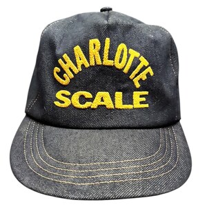 Puede incluir: Gorra de béisbol de mezclilla negra con las palabras "CHARLOTTE SCALE" bordadas en amarillo. La gorra tiene una visera curva y un botón en la parte superior. Las costuras son de hilo amarillo.