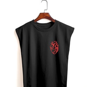 May include: Black sleeveless shirt with a red anatomical heart graphic on the front. The shirt is hanging on a wooden hanger against a white background. The graphic is a detailed illustration of a human heart.