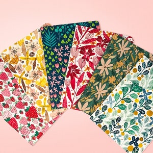 May include: Six different patterned cards with floral and geometric designs. The cards are arranged in a fan shape, with the top card being a dark green card with white flowers and gold accents. The other cards feature patterns of strawberries, flowers, and leaves in various colors.