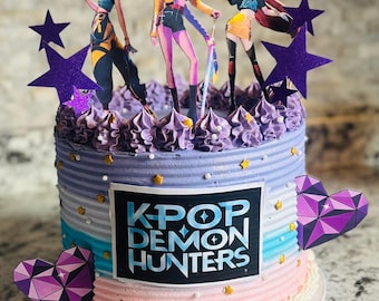 Könnte beinhalten: Ein mehrschichtiger Kuchen mit K-Pop-Thema. Der Kuchen hat einen Farbverlauf aus Rosa, Blau und Lila und ist mit stern- und herzförmigen Aufsätzen verziert. Der Kuchen ist mit Figuren von drei Anime-Charakteren gekrönt. Der Text "KPOP DEMON HUNTERS" ist auf der Vorderseite zu sehen.