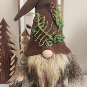 May include: A brown gnome with a long brown beard and a brown hat decorated with green moss and ferns.