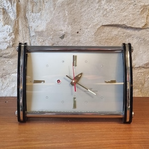 Puede incluir: Un reloj rectangular vintage con esfera plateada, marco negro y cromado y segundero rojo. El reloj tiene un diseño retro con esfera plateada e indicadores de hora dorados. El reloj está etiquetado "MADE IN CHINA".