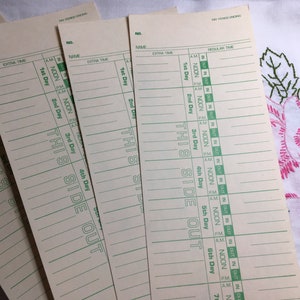 May include: A stack of vintage time cards with green ink. Each card has lines for name, extra time, and regular time, with "THIS SIDE OUT" printed vertically. The cards are on a white surface.