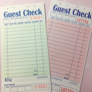 May include: Two guest checks with the words "Guest Check" in blue. One is pale green with the number 518501 in red, and the other is pink with the number 107706 in red. Both have lines for order details.