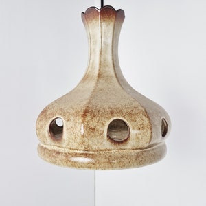 May include: A ceramic pendant light fixture with a brown and cream glaze. The light has a round, bell-shaped shade with several holes around the bottom.