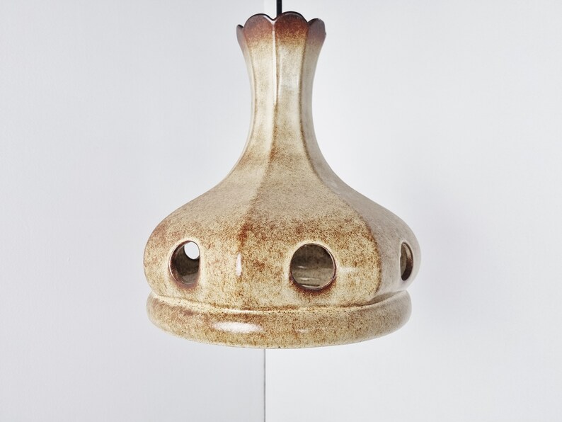 May include: A ceramic pendant light fixture with a brown and cream glaze. The light has a round, bell-shaped shade with several holes around the bottom.