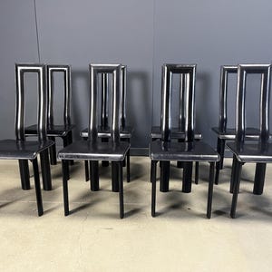 May include: Eight black chairs with square seats and tall, rectangular backs. The chairs have a minimalist design with a sleek, modern aesthetic. The legs are straight and the seats appear to be made of a smooth material.