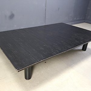 May include: A rectangular black coffee table with a textured surface and four cylindrical legs. The table is made of wood and has a minimalist design. The table is approximately 122 cm long and 61 cm wide.