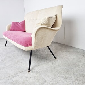 May include: A white and pink corduroy sofa with black metal legs. The sofa has two pillows, one pink and one white.