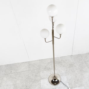 May include: A silver floor lamp with four white globe-shaped shades. The lamp has a long, slender stem and a circular base.