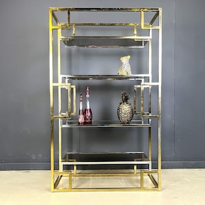 May include: A gold and silver metal shelving unit with five glass shelves. The unit has a geometric design and is decorated with a small gold pineapple and a gold leopard figurine.