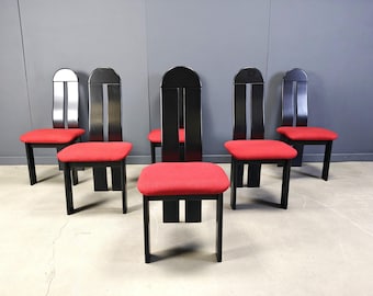 May include: Six black wooden chairs with red upholstered seats. The chairs have a distinctive design with a tall, arched back and vertical cutouts. The seats are square and the legs are straight. The chairs are arranged in a group.