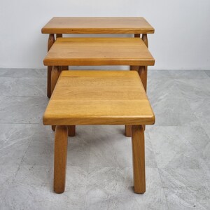Puede incluir: Conjunto de tres mesas nido de madera con acabado en madera natural. Las mesas son cuadradas y tienen patas simples y robustas.