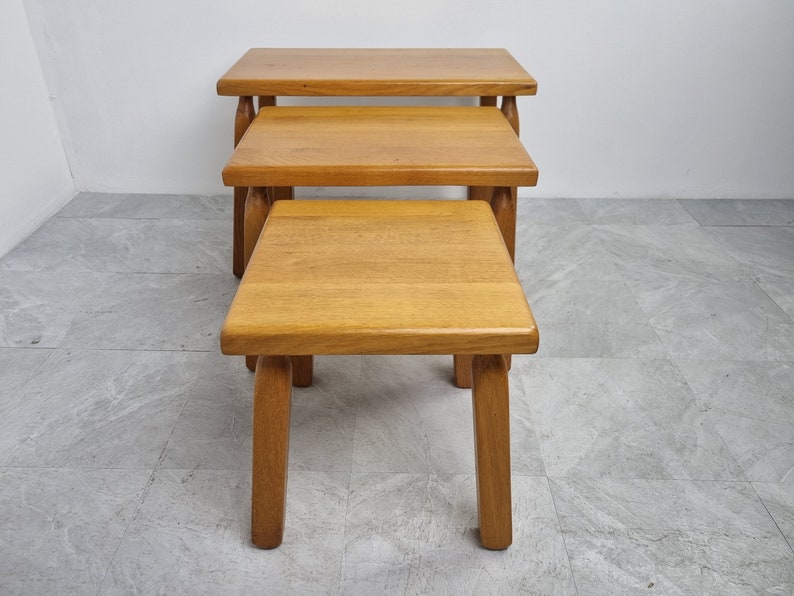 Puede incluir: Conjunto de tres mesas nido de madera con acabado en madera natural. Las mesas son cuadradas y tienen patas simples y robustas.