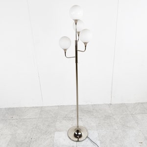 May include: A silver floor lamp with five white globe-shaped shades. The lamp has a long, slender stem and a round base.