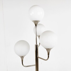 May include: A silver floor lamp with four white globe-shaped shades. The lamp has a modern design with a central pole and curved arms.
